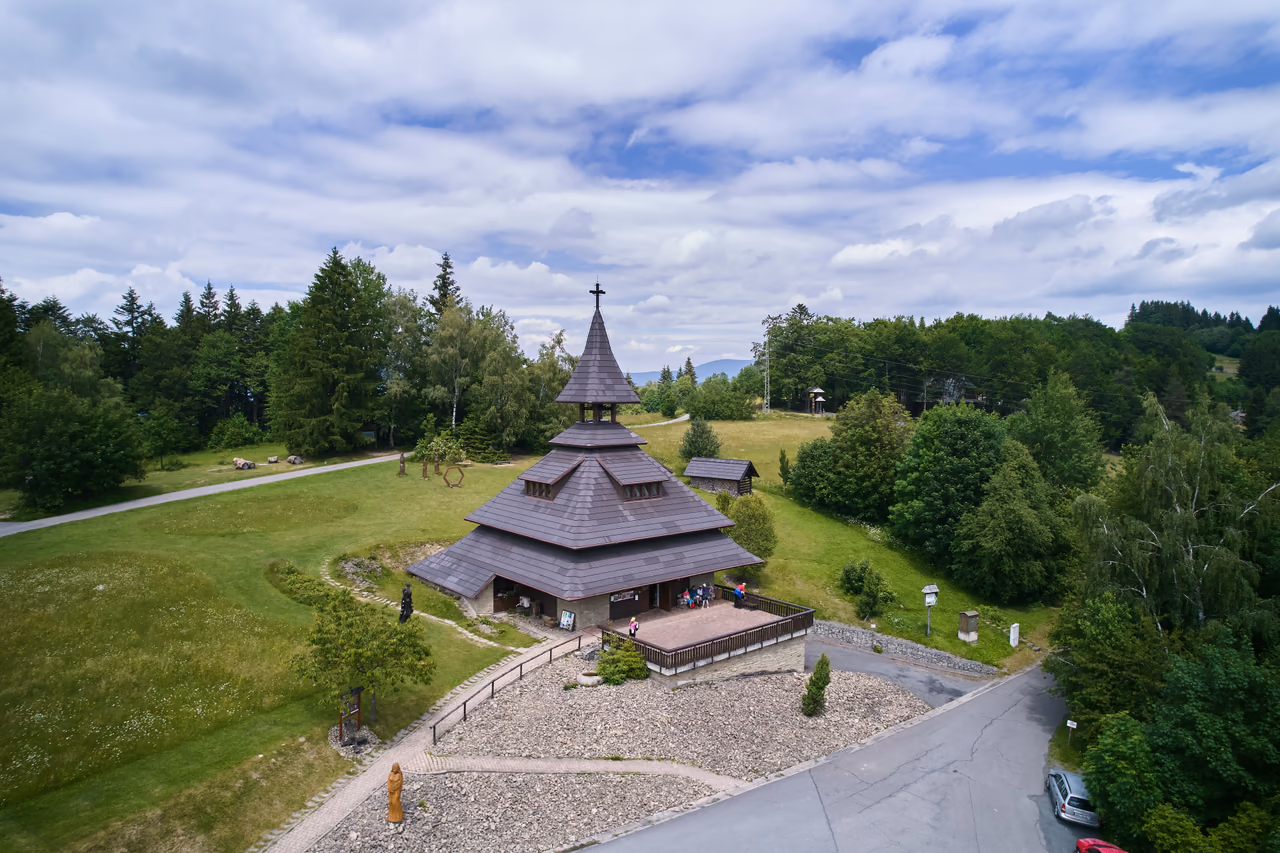 The Soláň bell tower on a grassy rise in the Čarták saddle, meadow and paths around it and wooded ridges behind