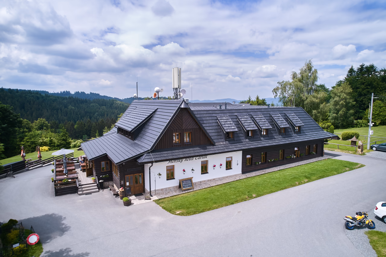 The front of the mountain hotel building in the Čarták saddle from above, meadows and tall trees around it