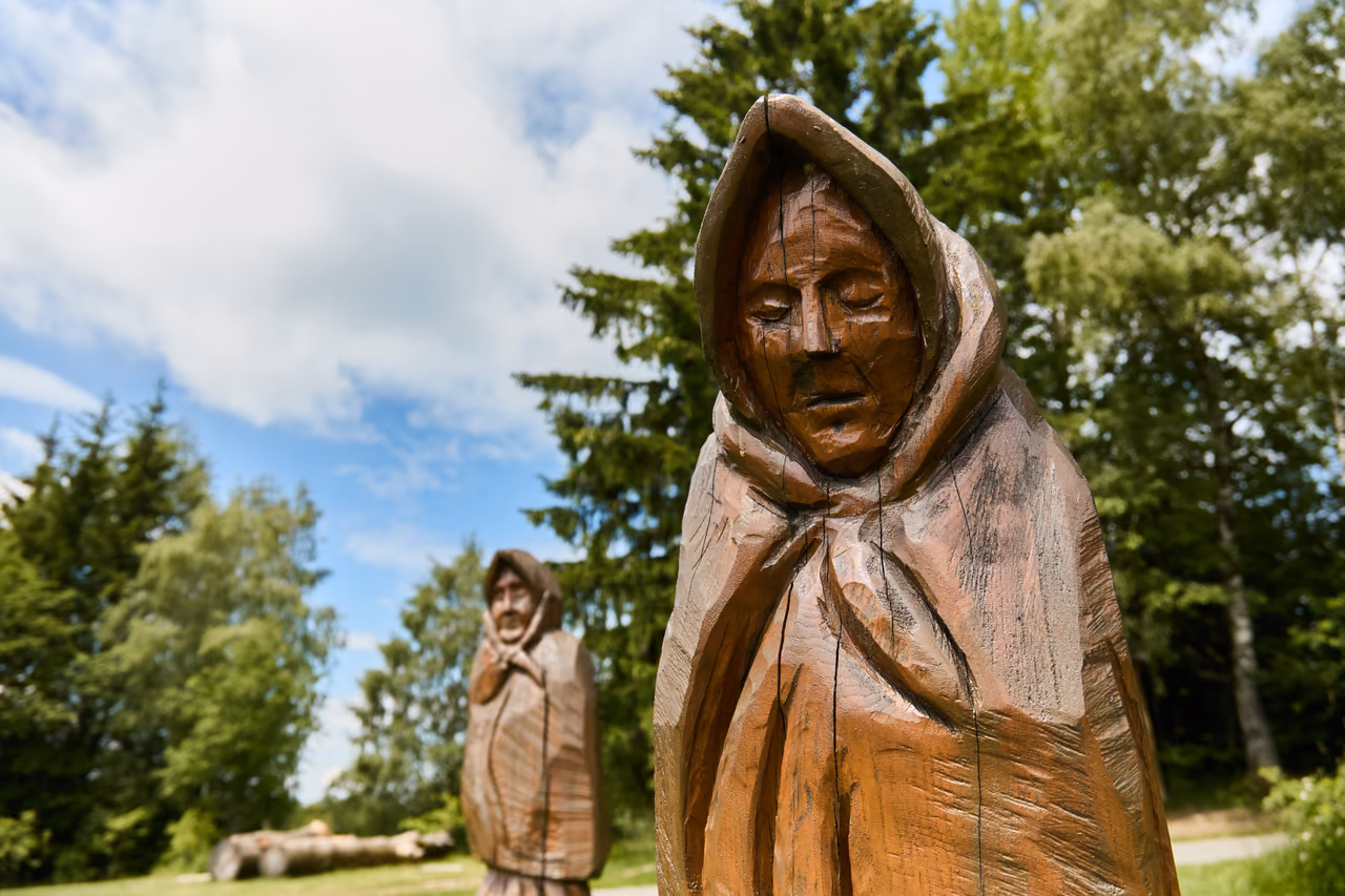 Detail of a wooden sculpture of a hooded figure, a second sculpture among the trees behind