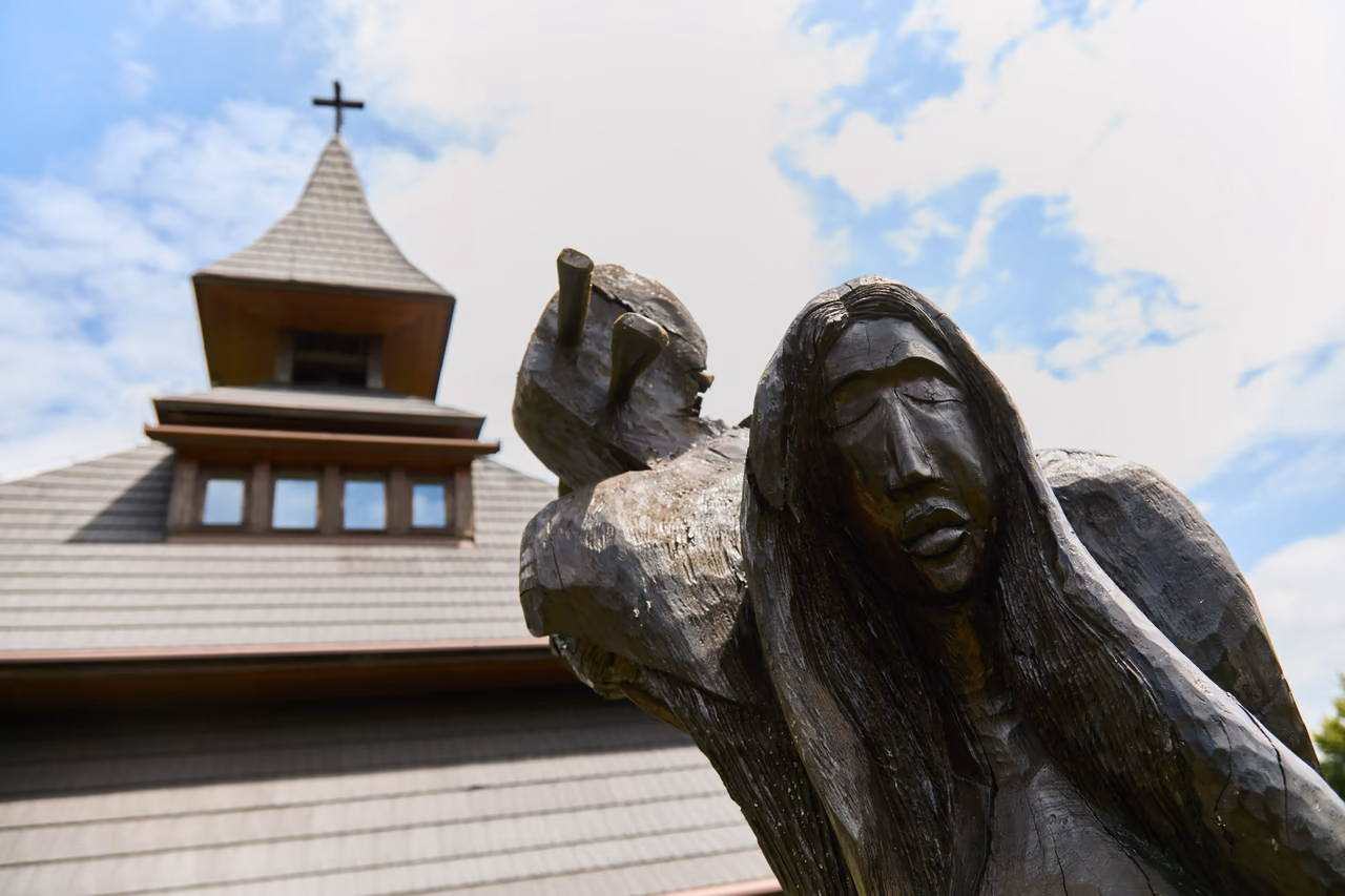A dark wooden sculpture of a figure with an animal on its shoulders, right by the bell tower