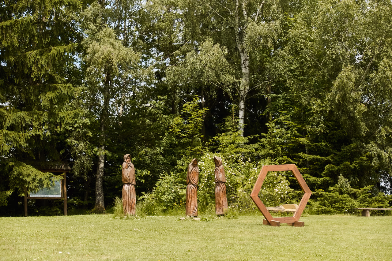 A group of wooden sculptures and a hexagonal frame on a meadow, trees behind