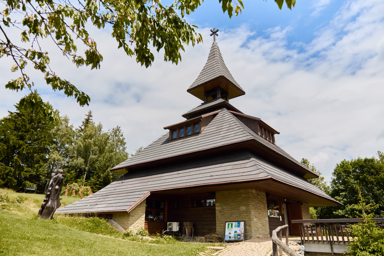 The Soláň bell tower from the foot of the slope, a wooden sculpture on the grass beside it