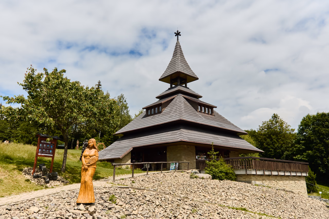 The Soláň bell tower with a wooden sculpture on the stone rise in front of the entrance