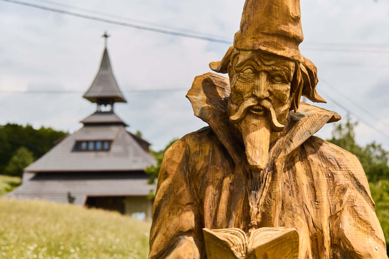 A sculpture of a bearded man in a pointed hat with an open book, the tower of the bell tower behind