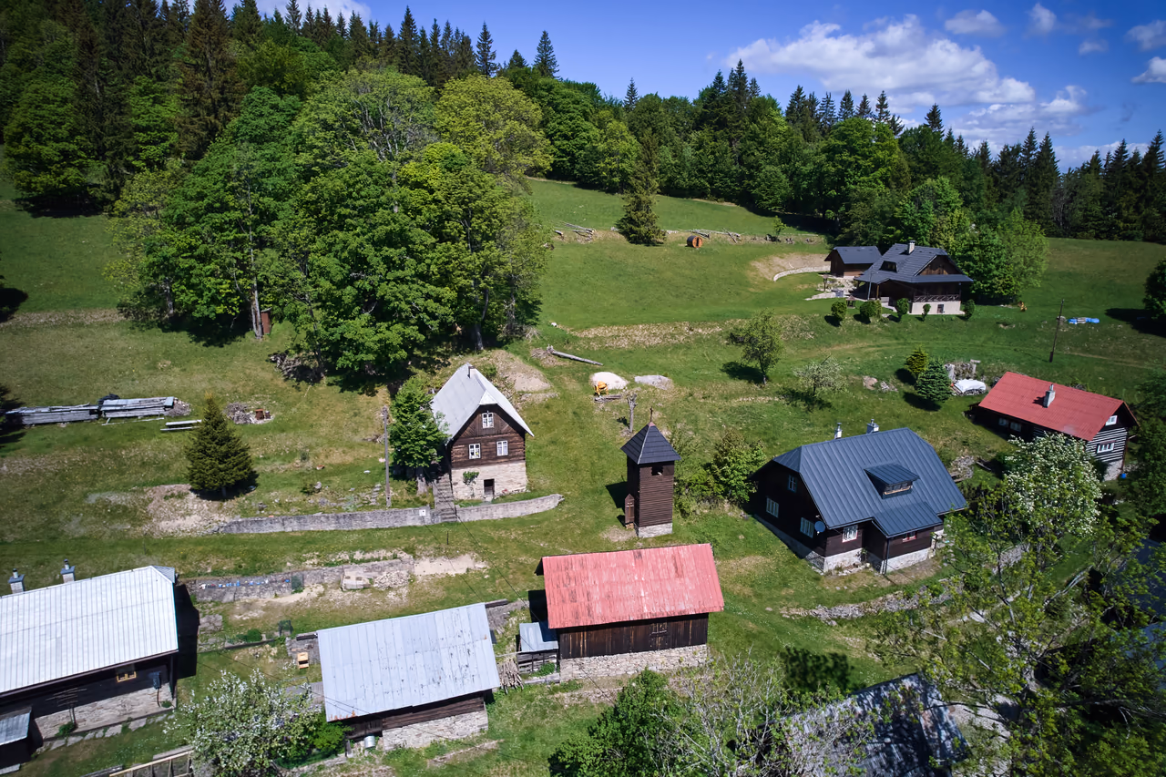 Letecký pohľad na osadu Greguše - zrubové chalupy a drevená zvonica na horskej lúke