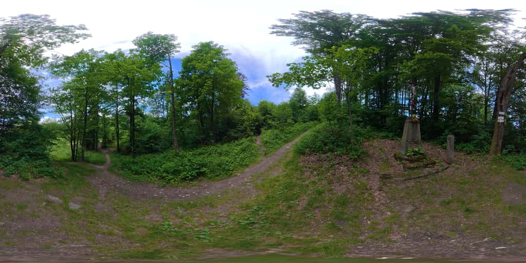 Kulová panoramatická fotografie palouku v sedle Hodorf - kříž na kamenném podstavci, hraniční kámen a turistický rozcestník mezi buky