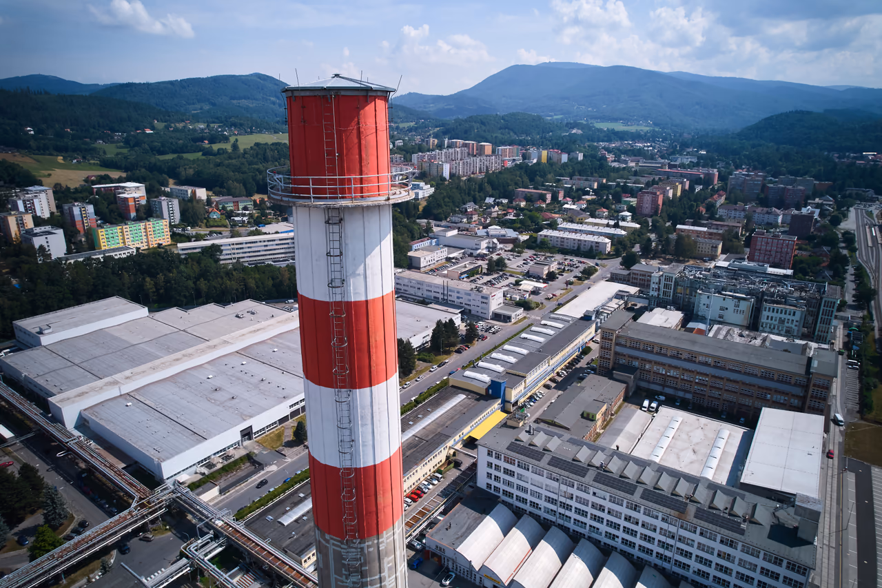 Vrchol vyššího komína s ochozem a žebříkem z dronu, v pozadí sídliště a hřeben Radhoště