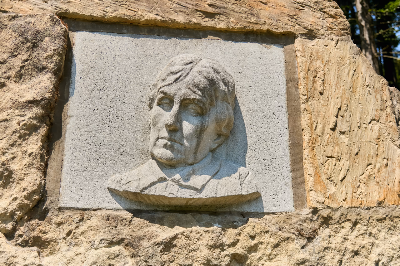 A close-up of a pale stone plaque with a relief of Charlotta Masaryková's head, set into a rough sandstone boulder