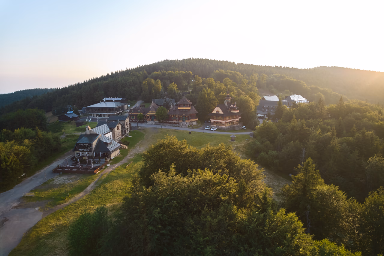 Podvečerný letecký pohľad na sedlo Pustevien - stavby lemujú hlavnú cestu, uprostred Jurkovičove útulne