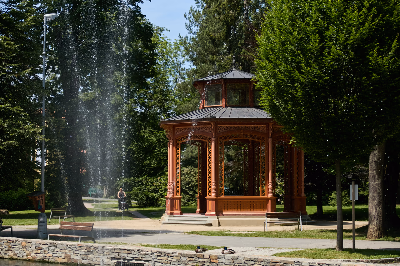 Altana muzyczna między drzewami parku, po lewej za nią tryska fontanna jeziorka