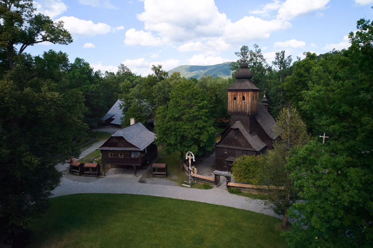 Kirche der hl. Anna mit Schindelturm mitten im Dřevěné městečko, dahinter ein Beskidenkamm