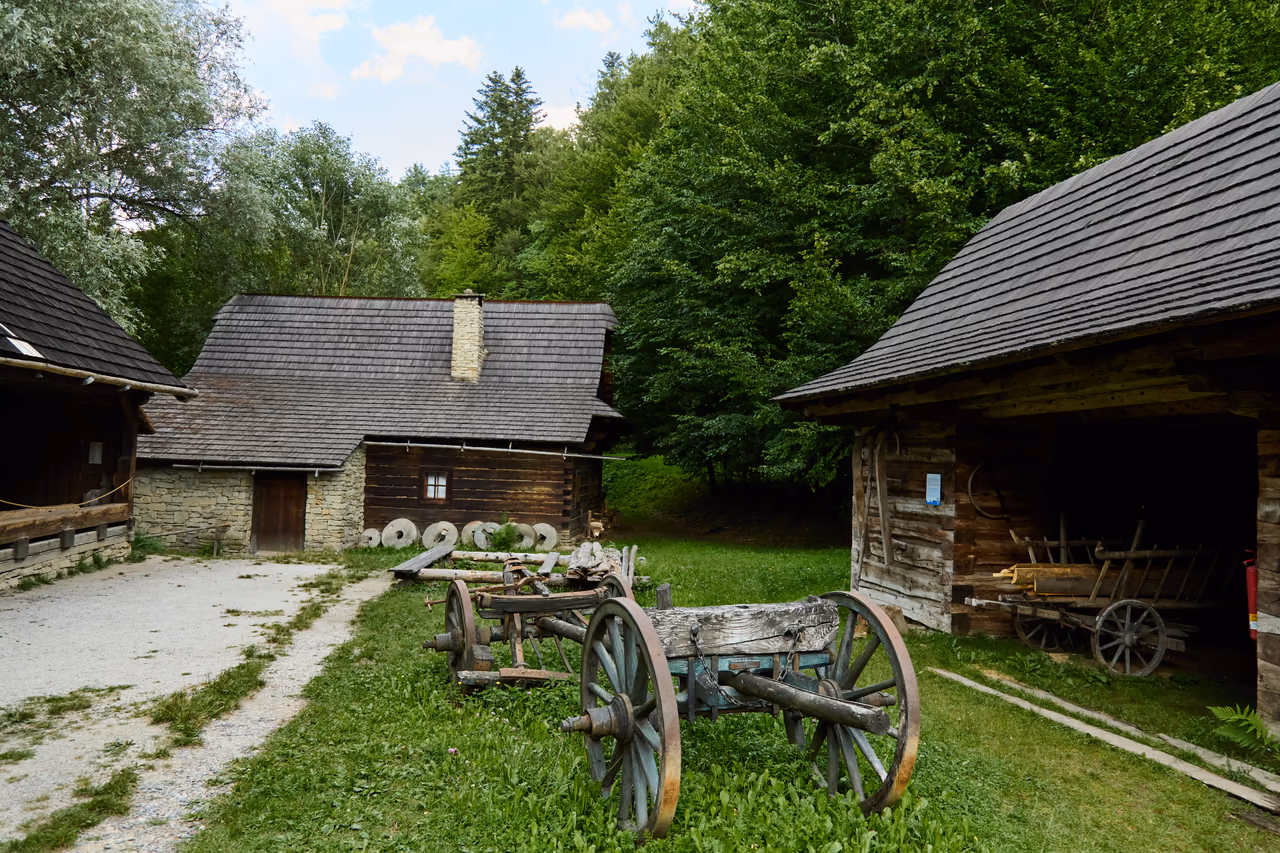 The yard of the Water Mill Valley – log buildings, old millstones and wooden wagons