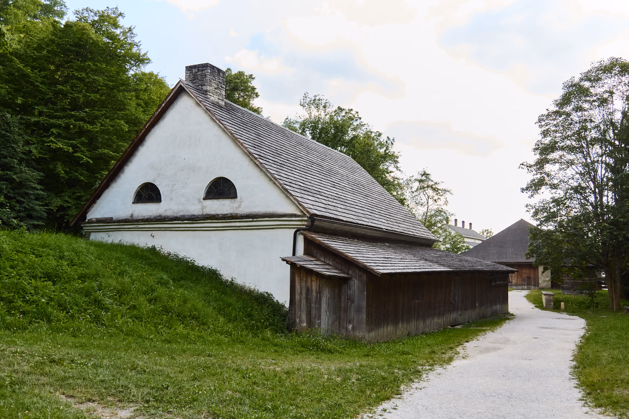 A white masonry building with a shingle roof and a wooden extension beside the valley lane