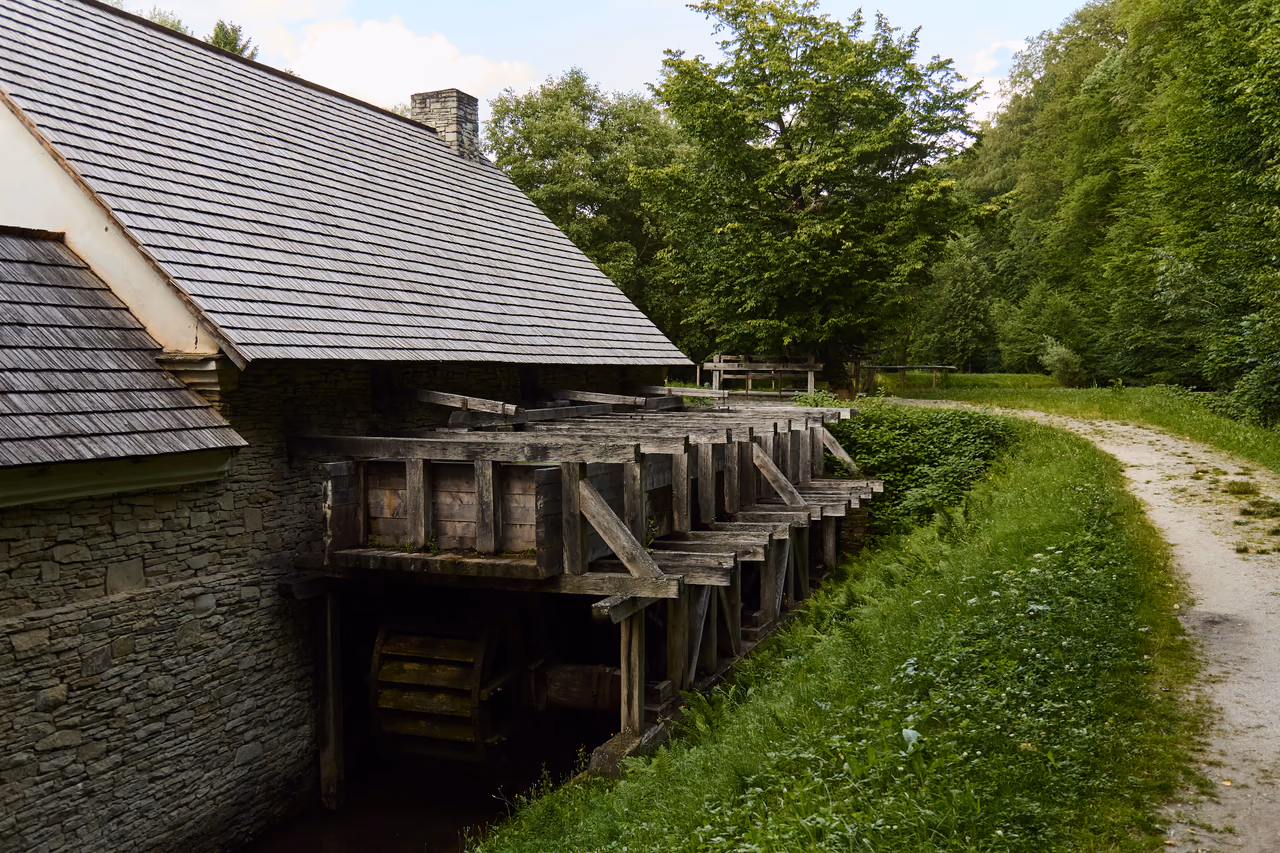 A stone building with a wooden millrace, a water wheel turning beneath its frame