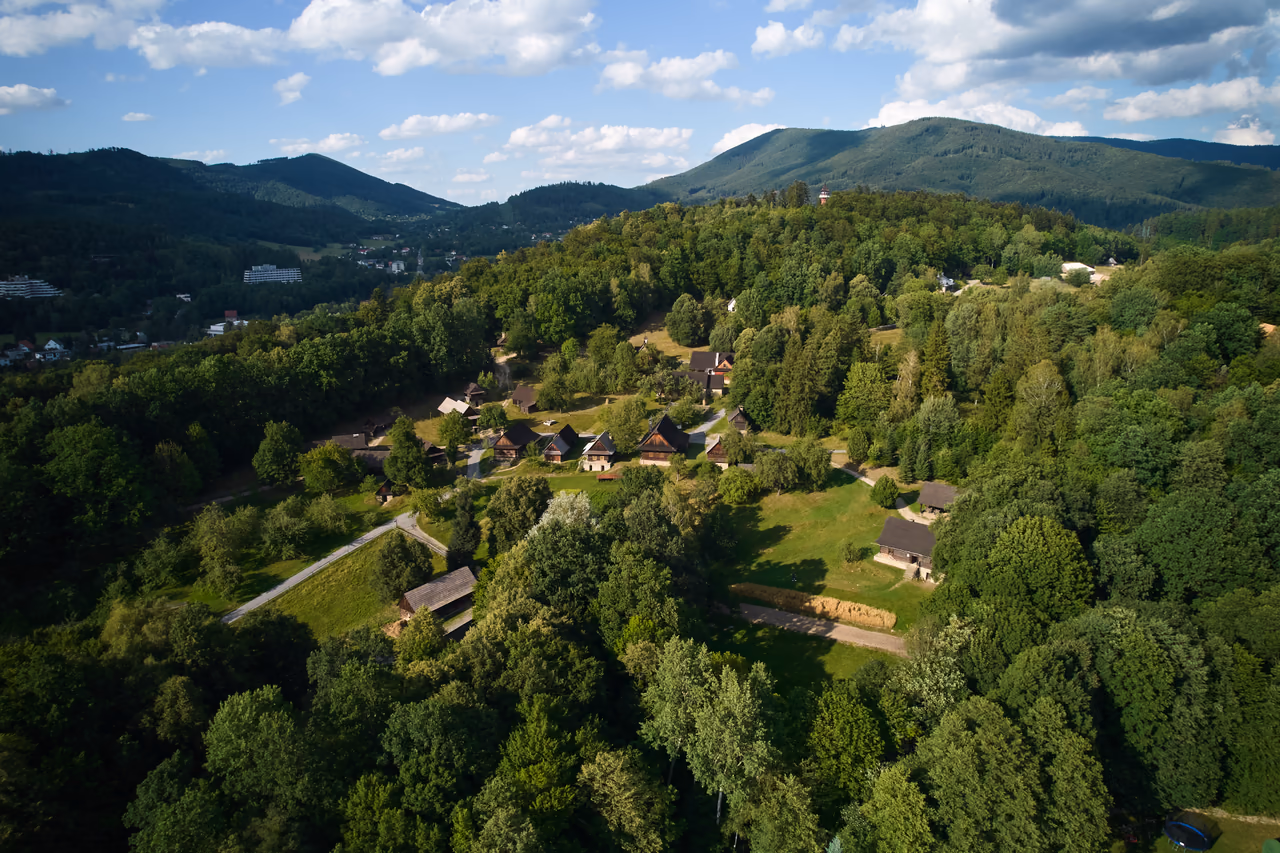 Aerial view of the Wallachian Village – log cottages scattered across a slope, with the Beskid hills behind