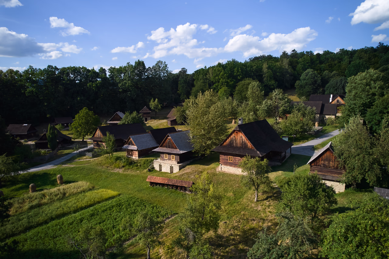 Aerial view of the Wallachian Village – log cottages on a grassy slope surrounded by forest