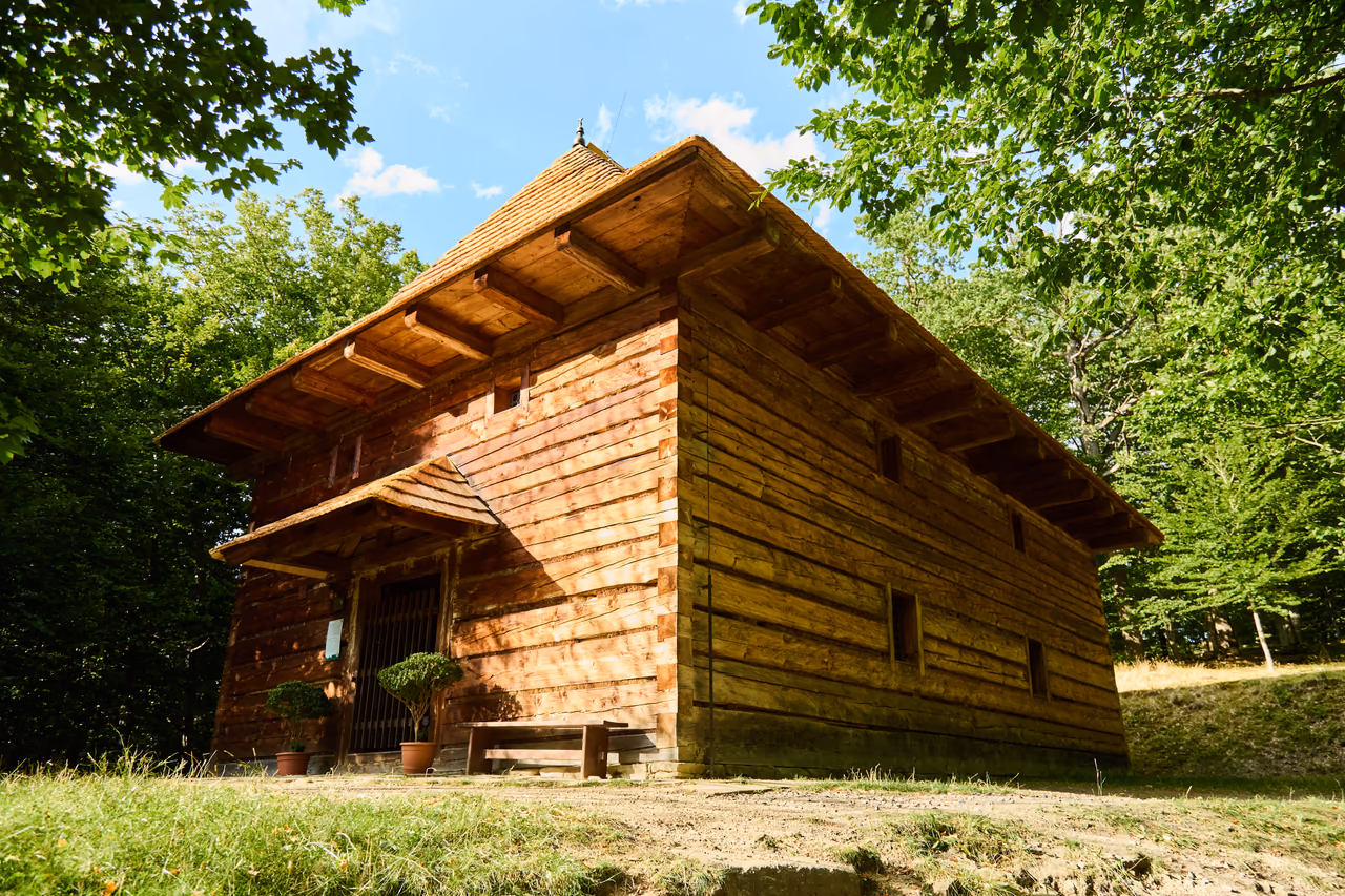 The log-built Protestant Toleration church with a shingle roof, an arcade above the entrance and a bench in front