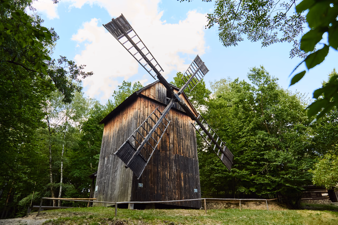 The windmill from Kladníky with its sails spread, a fence and broadleaved trees around it