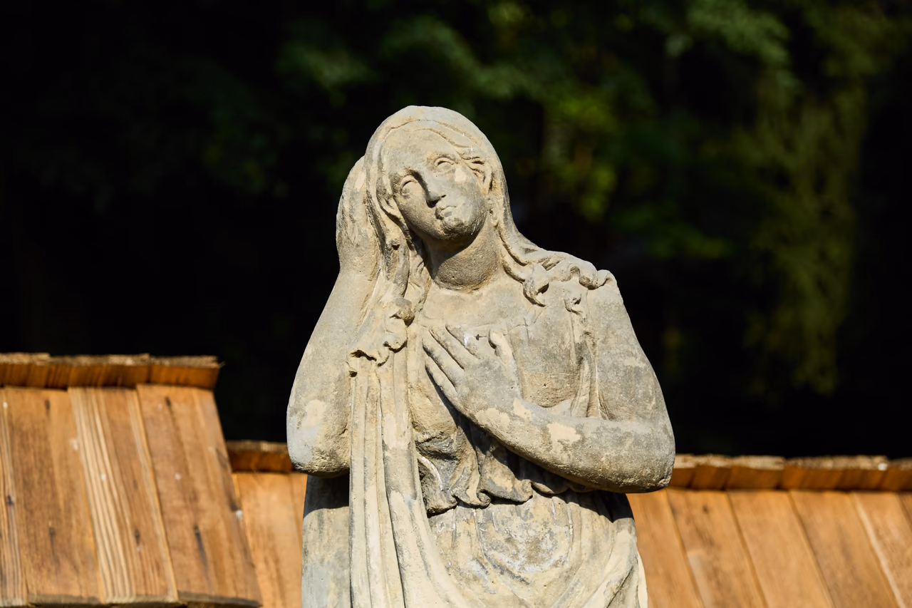 Steinerne Figur einer trauernden Frau mit Schleier über dem Kopf und einer Hand auf der Brust