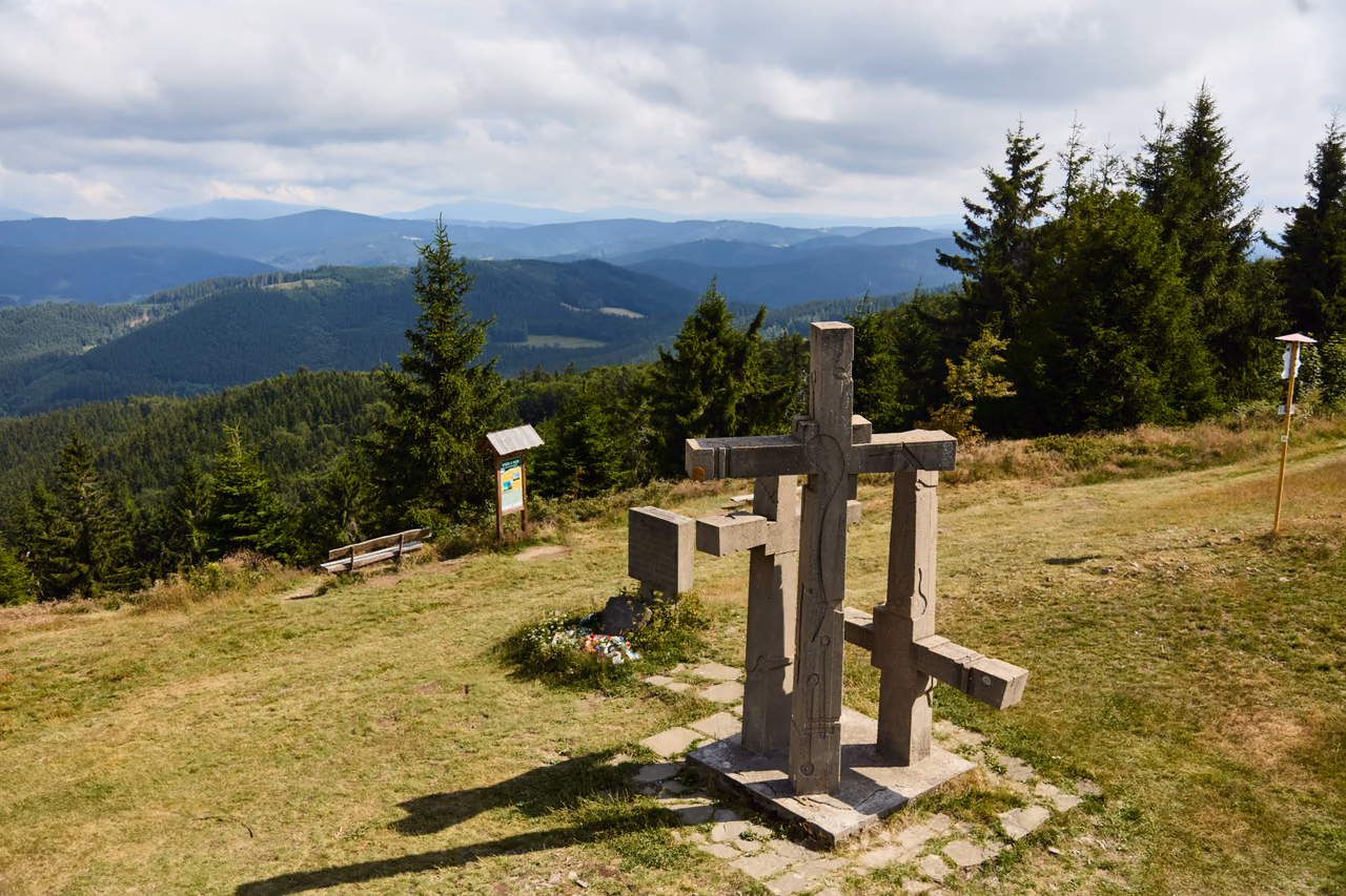 Tři kříže na vrcholové mýtině, vlevo informační tabule, v pozadí hřebeny Vsetínských vrchů