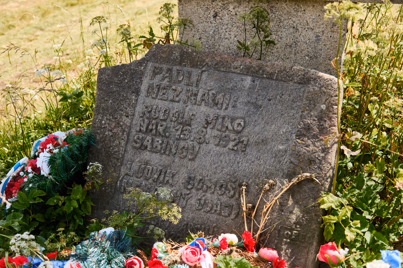 Detail nízkého kamene s vytesaným nápisem Padlí neznámí: Rudolf Miko, Ludvík Somoši; vlevo věnec v národních barvách